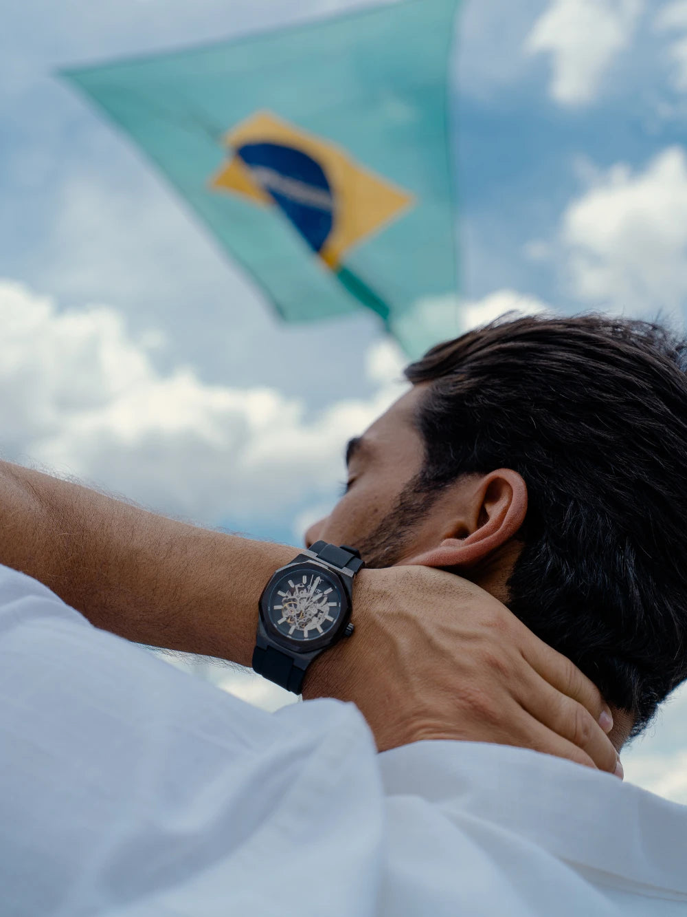 Homem com relógio automático masculino CURTT no pulso diante da bandeira do Brasil — marca brasileira de relógios